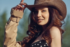 Girl in a cowboy hat resting in the village near the stables, portrait of a woman in the sun, rustic style. Portrait of a sexy brunette in nature. Perfect makeup, natural cosmetics